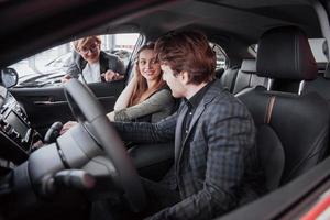 feliz hermosa pareja está eligiendo un coche nuevo en el concesionario foto