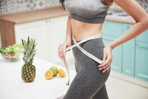 retrato de una mujer midiendo su cuerpo delgado sobre un fondo de cocina. concepto de fitness y estilo de vida saludable foto