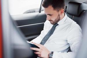 un joven empresario arregla sus asuntos con un bloc de notas mientras está sentado en la parte trasera del automóvil
