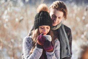Photo of happy man and pretty woman with cups outdoor in winter. Winter holiday and vacation. Christmas couple of happy man and woman drink hot wine. Couple in love