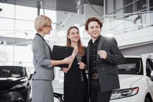 comprando su primer auto juntos. Un alto ángulo de vista del joven vendedor de automóviles de pie en el concesionario y contar las características del automóvil a los clientes. foto