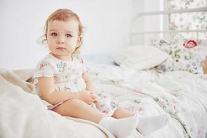 Baby girl in cute dress siting at bed playing with toys by the home. White vintage childroom. Childhood concept photo