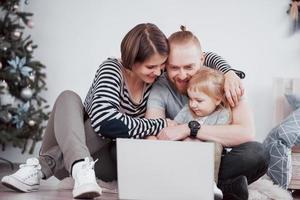 Familia de tres jóvenes usando la computadora portátil mientras está acostado sobre una alfombra en casa foto