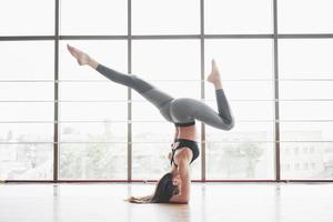 una mujer deportiva que está haciendo clases de yoga, estirando las piernas cerca de la ventana grande