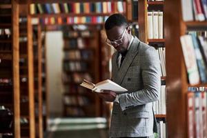 un hombre afroamericano en un traje de negocios de pie en una biblioteca en la sala de lectura. foto
