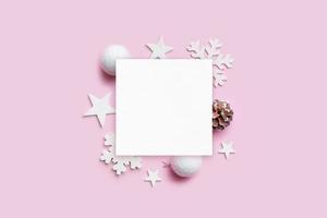 maqueta de tarjeta de felicitación navideña con adornos navideños en un escritorio rosa pastel. papel en blanco para texto de saludo. vista superior, plano foto