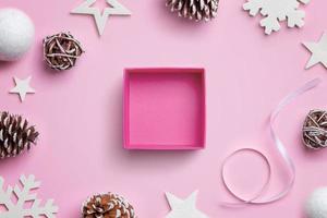Abra la caja de regalo de Navidad en el escritorio rosa, rodeada de adornos navideños. concepto de envoltura de regalo foto