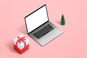 Concepto de compras navideñas con maqueta de portátil y regalo al lado de escritorio rosa pastel foto