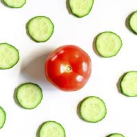 repeating pattern of sliced semicircles of fresh raw vegetable cucumbers for salad and a whole tomato photo