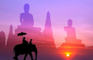 silhouette elephant with tourist with big buddha background at sunset photo