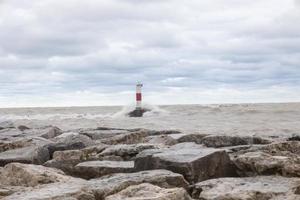 Waves crashing over lighthouse wall on lake Michigan in Kenosha, stone wall with clouds during a gale-force storm along the Wisconsin coastline causing flooding and damage to harbors and Marinas photo