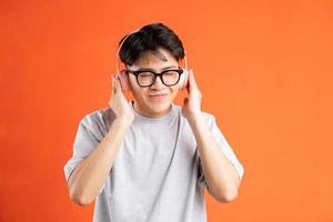 Portrait of young asian man listening to music with headphones, isolated on orange background