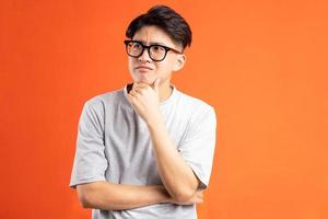 Portrait of young asian man thinking, isolated on orange background