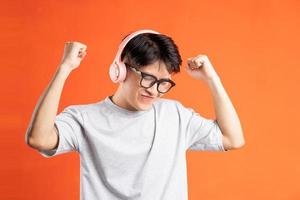 Portrait of young asian man wearing headphones and dancing, isolated on orange background