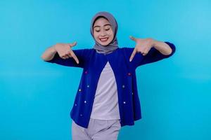 Good looking charismatic young woman with wearing hijab pointing down isolated on light blue background photo