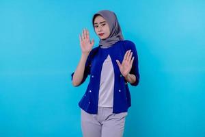 portrait of a woman wearing hijab showing stop gesture on blue wall photo