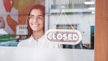 Feliz niña de pequeñas empresas cambiando de signo cerrado a abierto en la ventana sonriendo mirando afuera foto