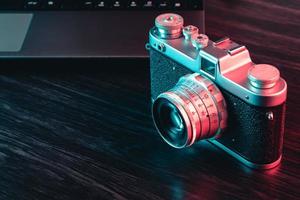 Old film camera and laptop on table. Blue and red light. view photo
