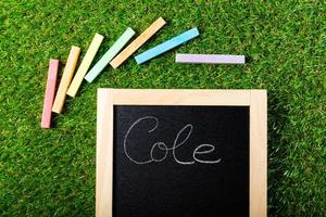 Top view of mini blackboard and colors on plastic grass background. Concept back to school. Cole is School in spanish photo