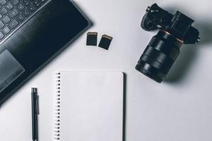 White office photography desk table with laptop, notebook, camera and pen. Top view with copy space. Mock up photo