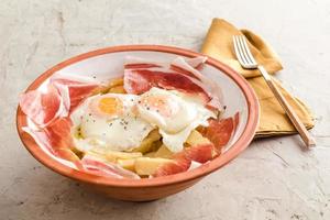 Broken fried eggs with potatoes and Iberian cured ham photo