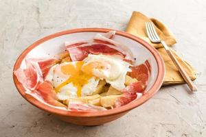 Broken fried eggs with potatoes and Iberian cured ham at spanish restaurant