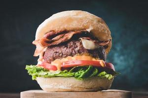 View of fresh tasty burger on wooden table. Hamburger with bacon, cheese, lettuce, tomato and sauce photo