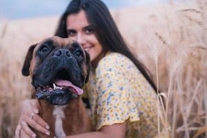 Close up view of a young happy woman hugging her dog in the middle of a wheat field. Nature and animals concept. photo