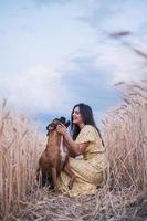 Portrait of a young woman hugging her dog in the middle of a wheat field. Nature and animals concept photo