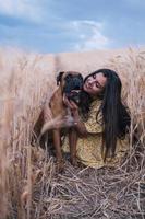 Portrait of a young woman hugging her dog in the middle of a wheat field. Nature and animals concept photo