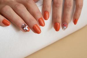 manos femeninas con manicura naranja con un patrón debajo de una parte superior brillante