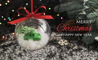 Merry christmas and new year on the background of a transparent ball with a toy car and a tree on the roof in the snow photo