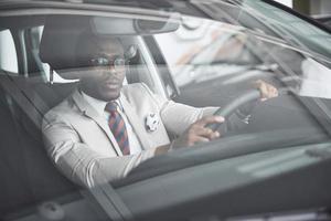 Vista frontal del apuesto hombre de negocios serio elegante africano conduce un coche foto