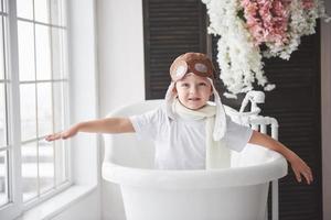 Happy kid in pilot hat playing in bathroom. Childhood. Fantasy, imagination. photo