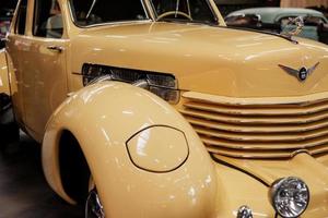 SINSHEIM, GERMANY - OCTOBER 16, 2018 Technik Museum. Headlight and hood. Right and front part of luxury creamy colored retro vehicle with motorbike at background photo