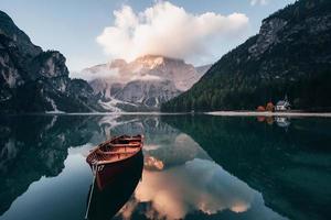 las nubes están en la parte superior. barco de madera en el lago de cristal con majestuosa montaña detrás. reflejo en el agua. la capilla está en la costa derecha foto