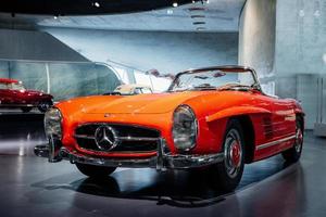 STUTTGART, GERMANY - OCTOBER 16, 2018 Mercedes Museum. Red and white vehicle behind. Beautiful orange colored retro car captured from the front photo