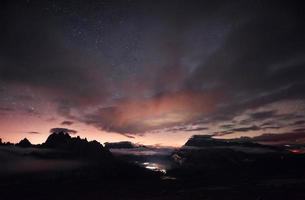 Something is shining in the middle of the forest. Beautiful space filled with stars in the sky. The mountains are surrounded by dense fog photo