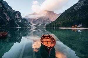 Looks like sun goes down. Wooden boats on the crystal lake with majestic mountain behind. Reflection in the water. Chapel is on the right coast photo
