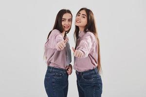 Pulgares hacia arriba. Dos hermanas gemelas de pie y posando en el estudio con fondo blanco. foto