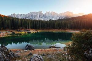 It's sunset time. Autumn landscape with clear lake, fir forest and majestic mountains photo