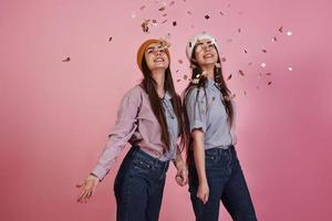 Holiday mood. New year conception. Two twins playing throwing golden confetti in the air in the studio with pink background photo