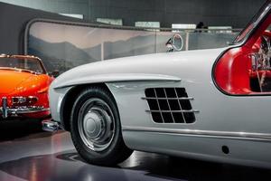 Photo from the side. Classic cars standing at black tile indoor on the automobile exhibition