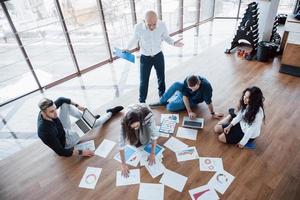 planificación de la estrategia en conjunto. equipo de negocios mirando papeles en el piso en busca de una idea. cooperación logro corporativo y concepto de trabajo en equipo foto