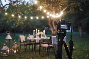 Professional equipment. Camera on the tripod stand in the field in front of prepared table at evening time photo