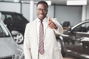 Young black businessman on auto salon background. Car sale and rent concept. photo