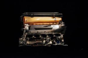 Una vista frontal de primer plano del motor de combustión interna de detalle de coche con parte naranja aislada sobre fondo negro foto