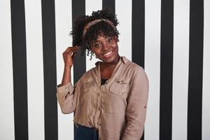 Sonrió niña afroamericana se para y toca su cabello en el estudio con líneas verticales blancas y negras en el fondo foto