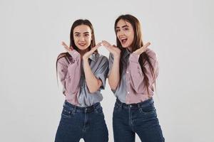 Playful mood. Two sisters twins standing and posing in the studio with white background photo