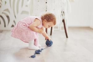 Childhood concept. Baby girl in cute dress play with colored thread. White vintage childroom